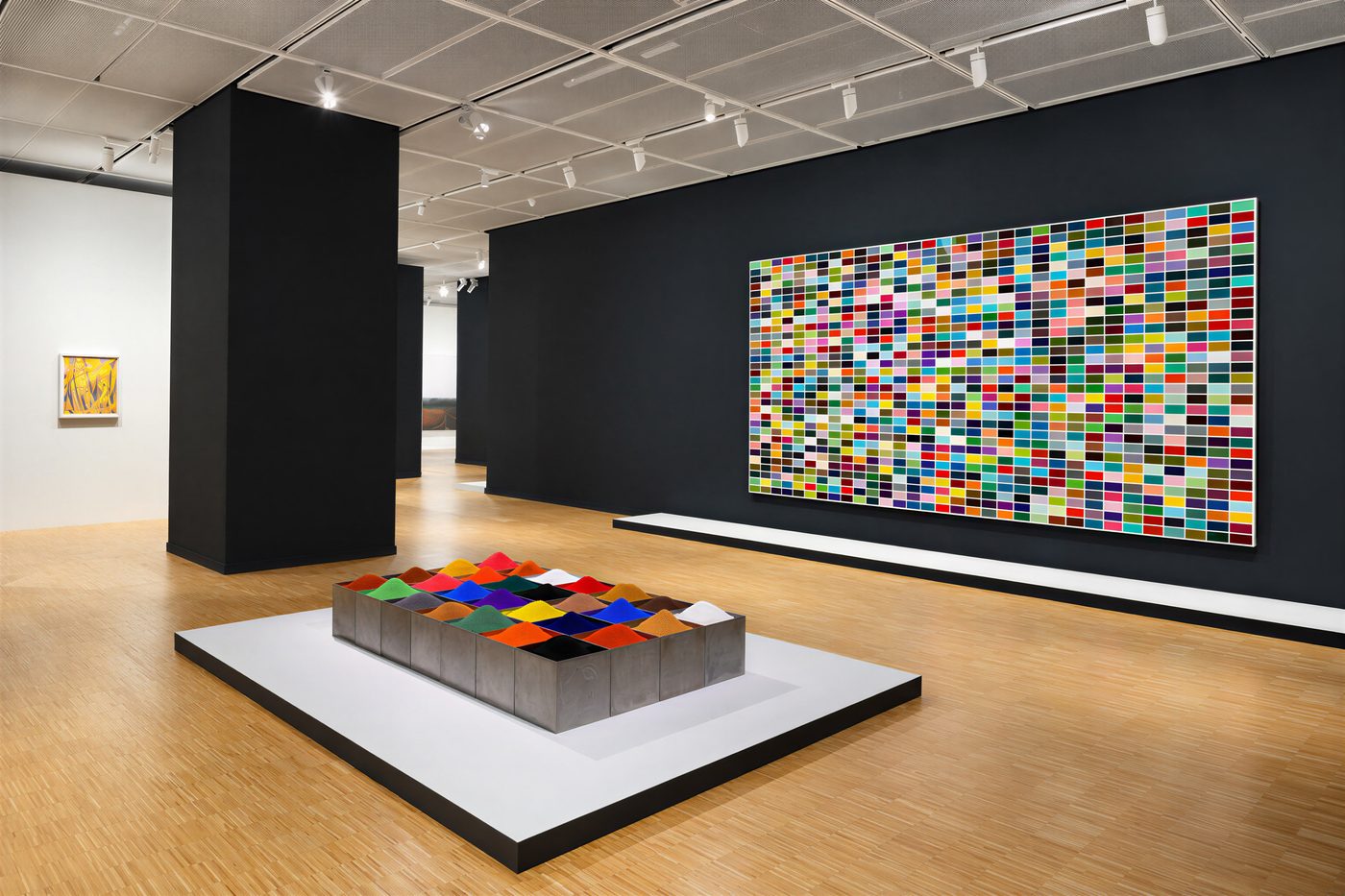 Siyah duvarlı salonda Gerhard Richter'in 1024 Farben tablosu ve önünde metal kutulara doldurulmuş renkli pigment yerleştirmesi
