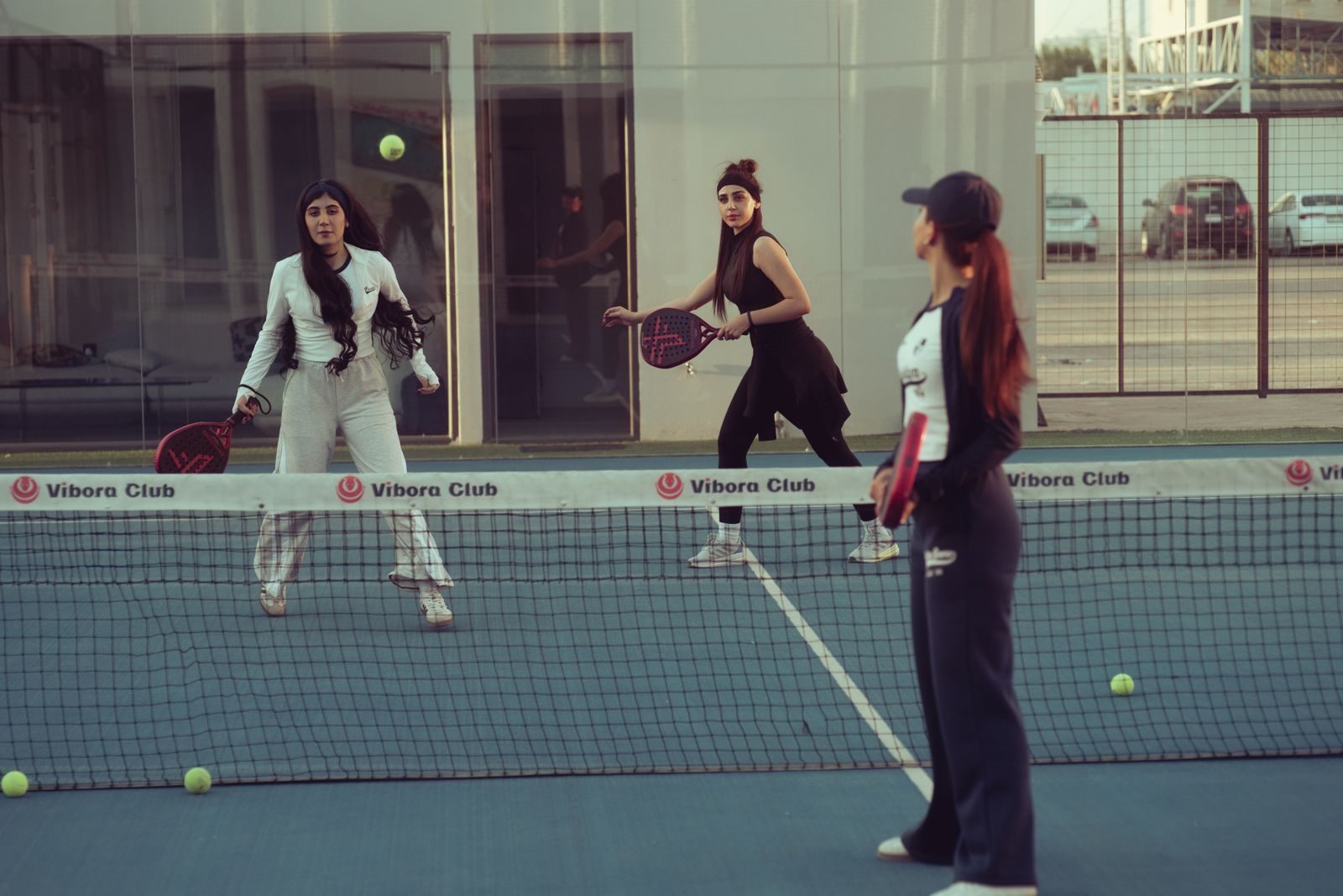 Cam duvarlarla çevrili bir padel kortunda çift olarak maç yapan oyuncular